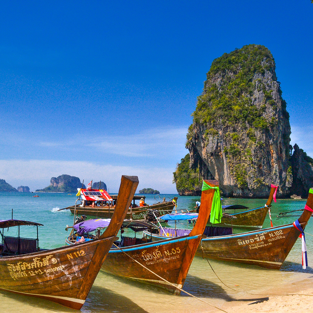 A beautiful sunny day with a group of Thai boats tied up on the shore.