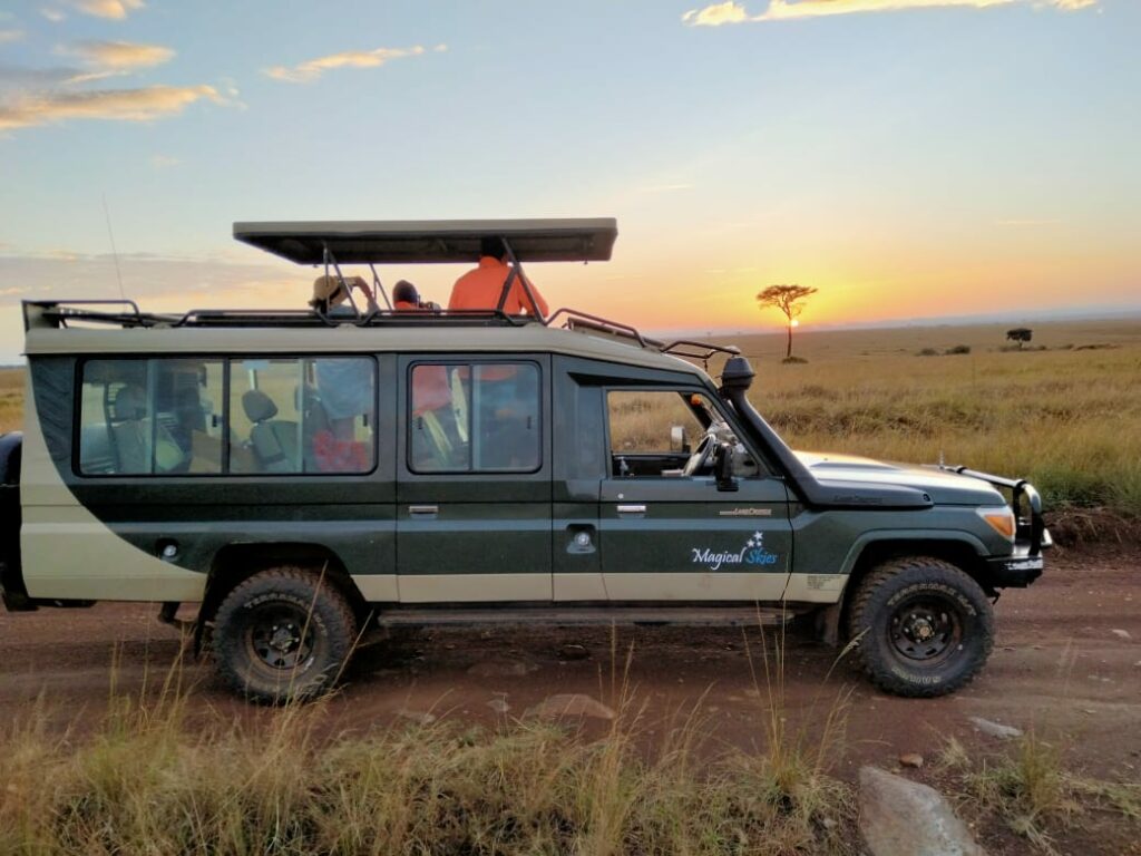 Magical skies 4x4 parked with people in it looking at the sunrise/sunset and taking photos of it. The sun is a beautiful glowing yellowy red.