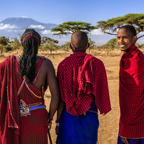 three Masai Mara tribe people. two of them looking into the distance and one looking at the camera. mount Kilimanjaro is in the background with a clear blue sky