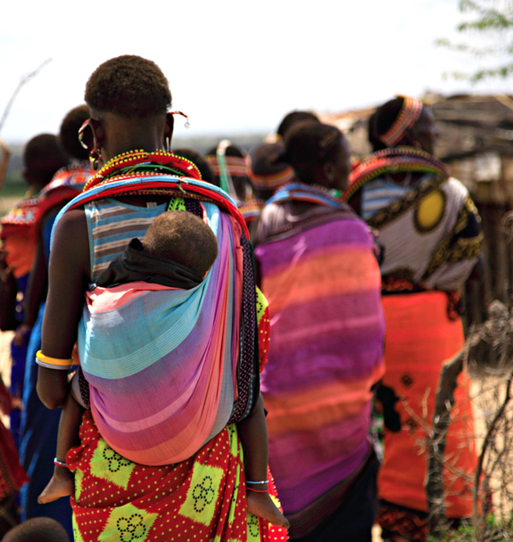 Group of Masai villagers walking away from the camera. All in their beautiful colourful garments with a baby on a lady's back.
